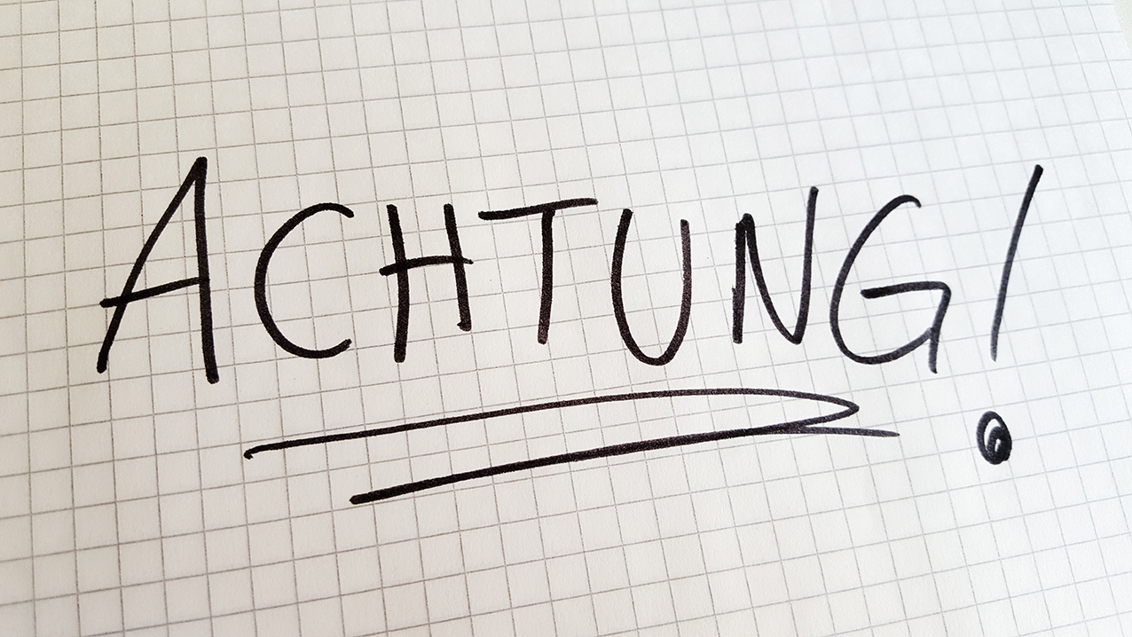 Auf einem karierten Blatt steht in Großbuchstaben: ACHTUNG!