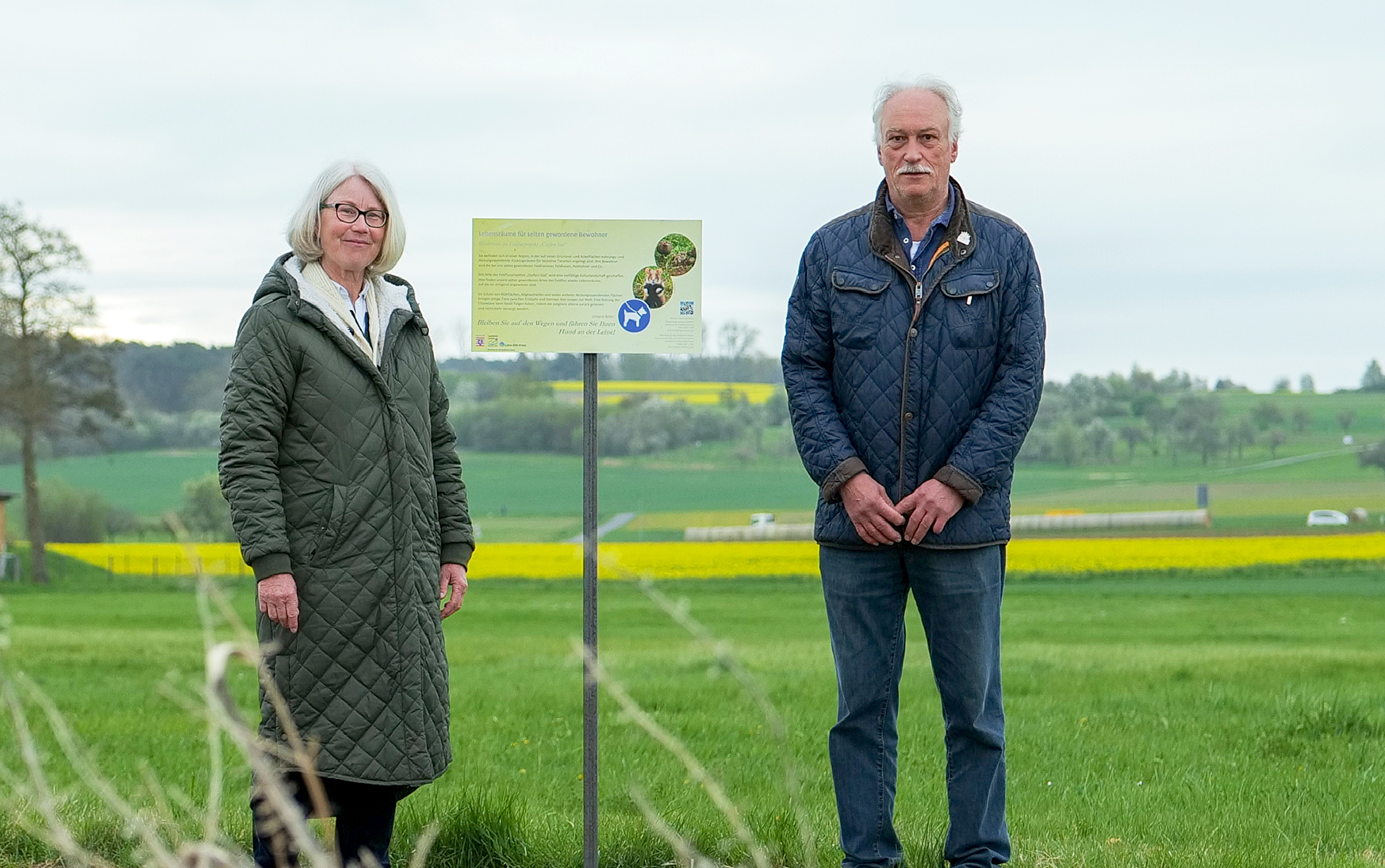 Seit kurzem machen Hinweisschilder auf den Tiernachwuchs im Feldflurprojekt „Gießen-Süd“ aufmerksam. Margot Schäfer, Leiterin der Abteilung für den ländlichen Raum, und Landwirt Hans-Otto Arnold sind bei der Aufstellung der Schilder dabei. Foto: Lahn-Dill-Kreis