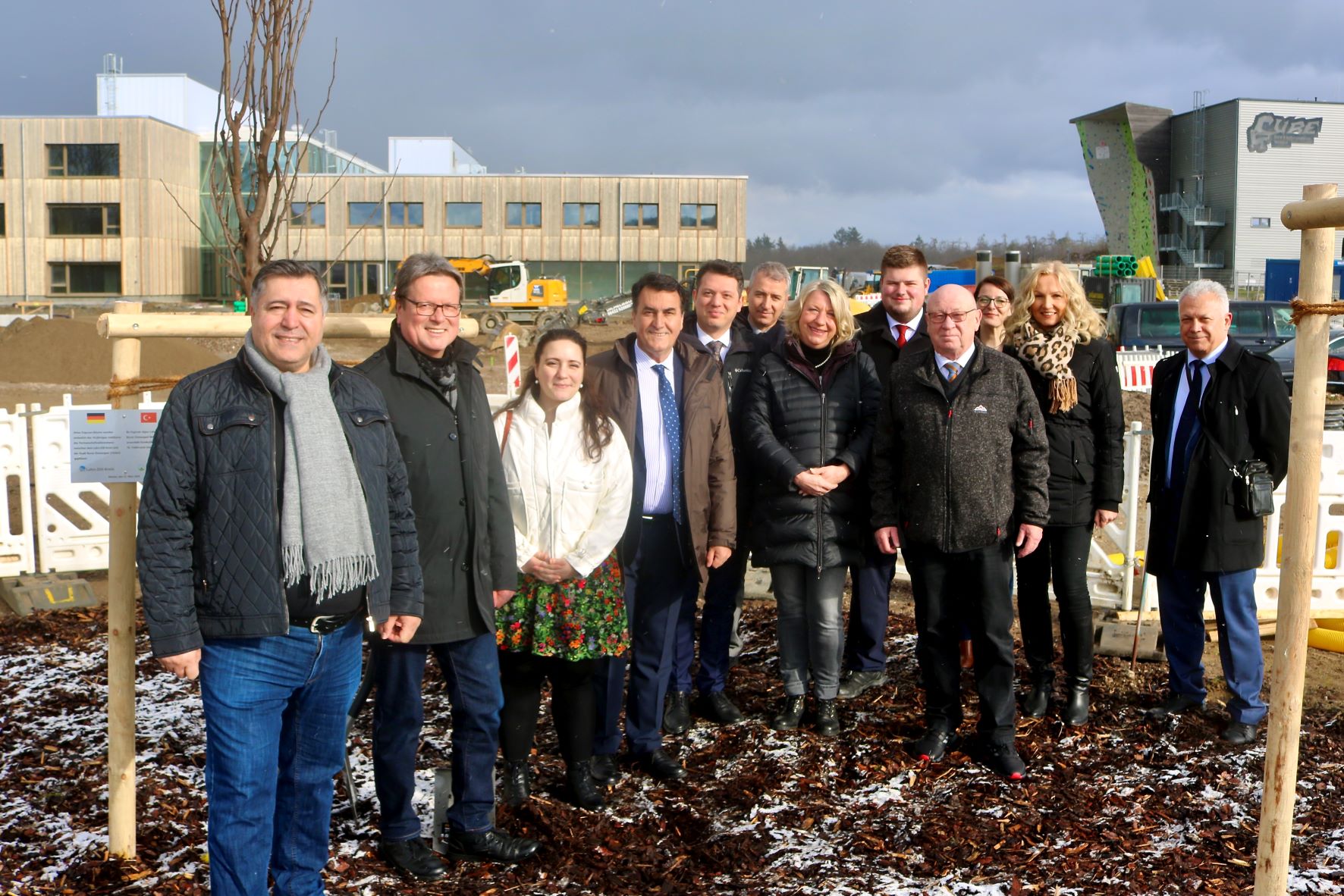 Verschiedene Vertreterinnen und Vertreter des Lahn-Dill-Kreises und der türkischen Delegation stehen neben dem neu gepflanzten Baum und lächeln in die Kamera.