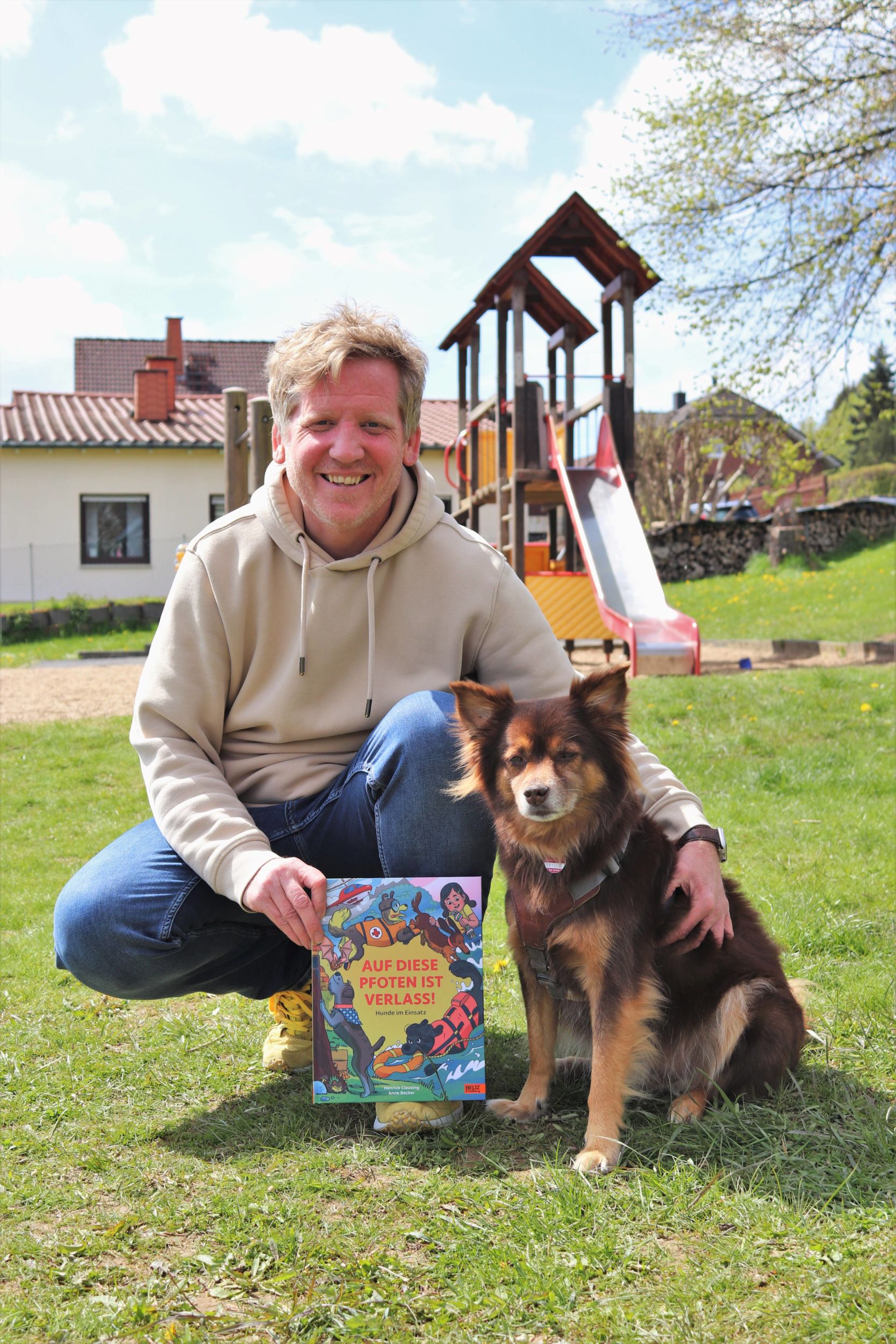 Begleitet wird der Autor Henrick Clausing von seinem Hund Filou, der als Trauerbegleithund ausgebildet ist. Die beiden posieren auf einer Wiese mit dem Buch. Foto: Lahn-Dill-Kreis/Judith Muhlberg